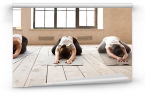 Five girls during yoga session at sport studio. Sportive females lying in row relaxing on wooden floor rubber mats doing Child Pose. Horizontal photography banner for website header. Wellness concept