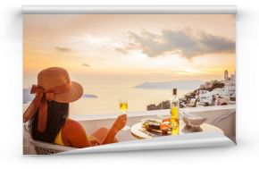 Female tourist enjoying food, wine and sunset view at Santorini, Greece