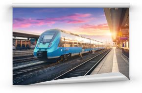 Modern high speed commuter train on the railway station and colorful sky with clouds at sunset in Europe. Industrial landscape with blue passenger train on railway platform. Railroad background