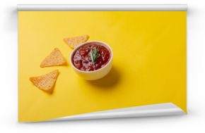 Red sauce with rosemary served in bowl with nacho chips on yellow background with copy space