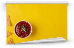 Red sauce with rosemary in bowl by nacho chips on yellow background with copy space