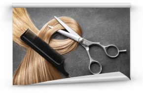 Nożyczki fryzjerskie z grzebieniem i pasmem blond włosów na szarym tle