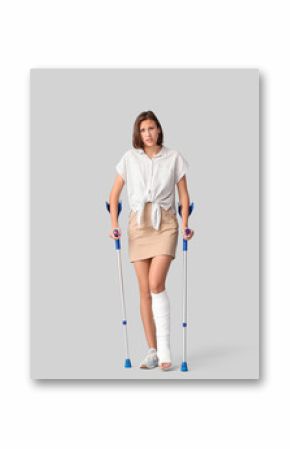 Young woman with broken leg and crutches on light background