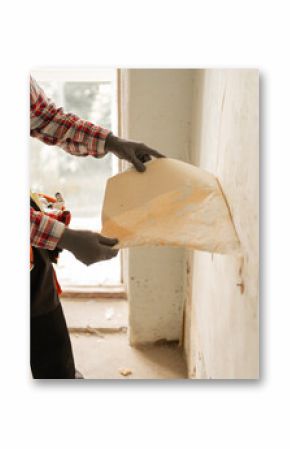 the hands of a master removing old wallpaper from a wall in an apartment before renovation