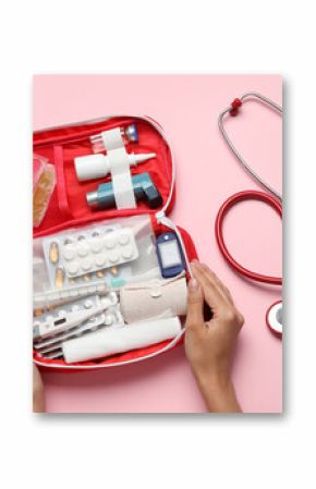 Female hands with first aid kit and pills on pink background