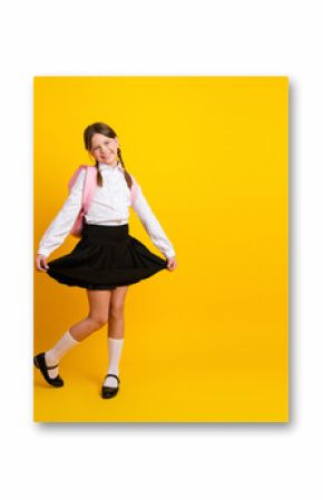 Adorable schoolgirl smiling in formal uniform against a bright yellow background, celebrating back-to-school season with joy
