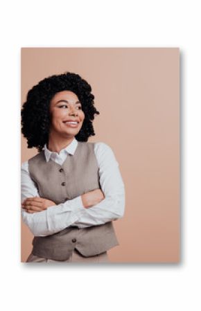 Confident young professional woman in formal attire with crossed arms posing on beige background with a charming smile