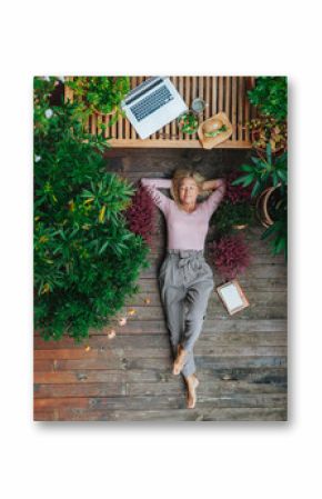 Tpp view of older woman working from homeoffice, lying on wooden patio.