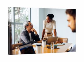 Two colleagues discussing work in an office with laptops and documents