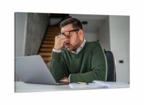 Stressed man experiencing headache while working on laptop