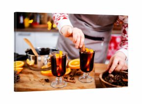 Woman garnishing hot mulled wine with cinnamon and star anise in christmas and new year kitchen creating warm aromatic holiday beverage with citrus and spicy winter notes