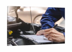 Auto check up and car service shop concept. Mechanic writing job checklist to clipboard to estimate repair quotation to client at workshop garage.