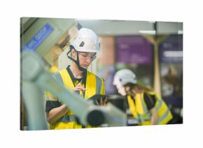 A female robotics engineer in an R and D lab uses a tablet to program an artificial intelligence cobot. She is inspecting the robotic system hardware and software diagnostics.