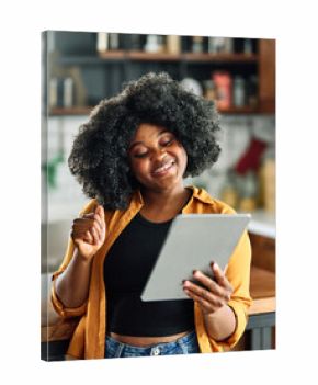 Happy young afro american woman having fun preparing food and looking for recipes online using a tablet in kitchen, or a young businesswoman working from home office making connections online
