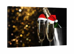 Sparkling wine in glasses with small Santa hats against blurred lights on black background