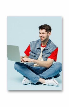Full body smiling fun young happy IT man wears denim vest red t-shirt casual clothes sit hold use work on laptop pc computer chatting online isolated on plain pastel light blue cyan background studio.