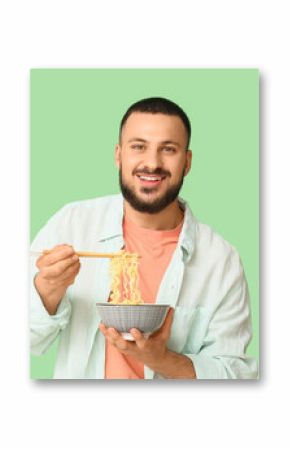 Young man eating tasty ramen on green background