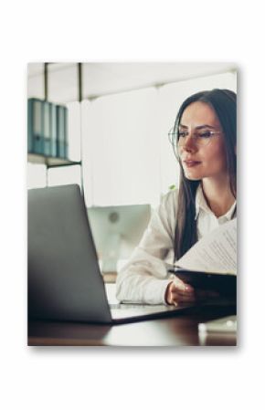 Professional businesswoman in formal attire working diligently at her office desk, reviewing documents and focusing on tasks.