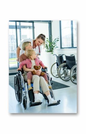 Female doctor pushing wheelchair with mother and son after treatment
