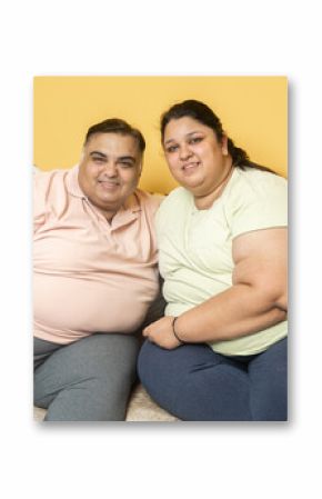 Smiling plus size indian couple looking at camera. Overweight husband wife sitting on couch. Fat chubby man and woman together. Obesity