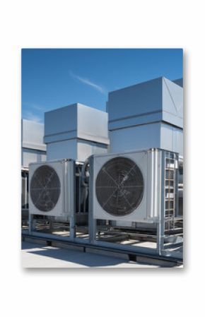 Multiple large industrial air conditioning and ventilation units are installed on the rooftop of a commercial building under a clear blue sky. 