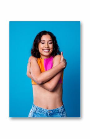 Young woman expressing self care and confidence wearing trendy casual outfit against vibrant blue background