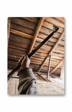 A person holding a crowbar inside an old wooden attic