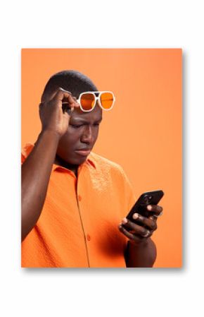 Black man, phone and confused in studio with chat, thinking and reading post on orange background. African person, smartphone and doubt with fake news, gossip and scroll choice on social network