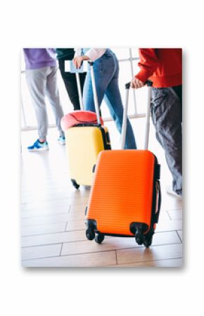 Group of young travelers walking with colorful luggage in an airport terminal on a bright day, preparing for a journey