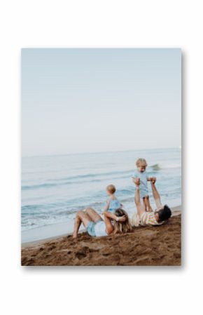 Parents lying in sand and having fun with kids on beach on summer holiday.