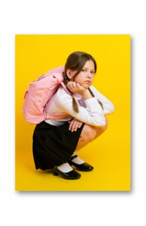 Schoolgirl sitting against bright yellow background wearing a school uniform and pink backpack, looking thoughtful and stylish