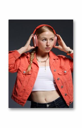 Beautiful woman in stylish bijouterie, headphones and jacket posing on dark grey background