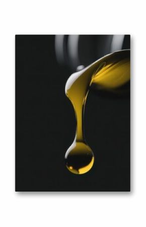 Close up of viscous yellow liquid, like cooking oil or engine lubricant, forming a perfect droplet against a dark isolated background