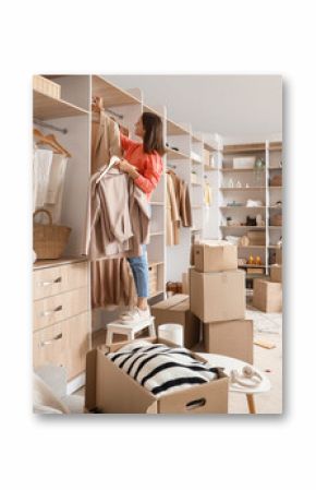 Young woman taking clothes from rack with wardrobe boxes in dressing room
