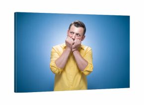 Worried young man biting her fingernail, she know the secret over blue background, dresses in yellow shirt
