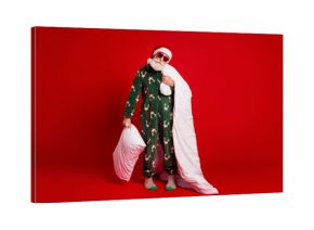 Playful Santa in festive pajama with blanket and pillow against a bold red backdrop