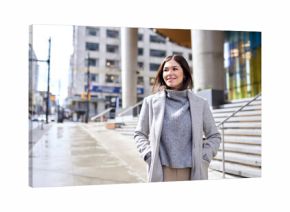 Young happy elegant brunette woman wearing coat standing on big city street. Smiling business lady walking outdoors looking away enjoying fall time in downtown on sunny day.