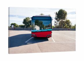 Modern red electric bus standing in a sunny empty parking lot, representing sustainable public transport and urban mobility