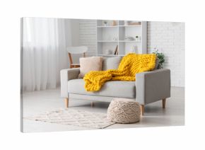 Modern interior of living room with stylish grey sofa, pouf and yellow knitted plaid