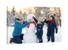Happy young family with two children building a snowman together in a snowy winter park.