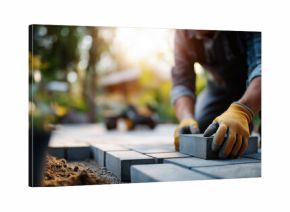 Faceless landscaper man laying interlocking paving stones creating new backyard patio defocused garden background wearing protective gloves work clothes outdoor hardscaping