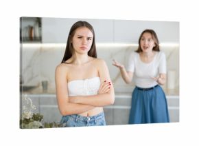 Upset teen girl standing in the kitchen, cross mother scolding her standing behind