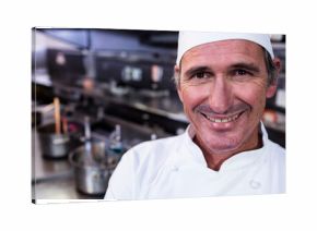 Smiling chef wearing white coat by steel countertop with pots, pans, utensils under hanging lights