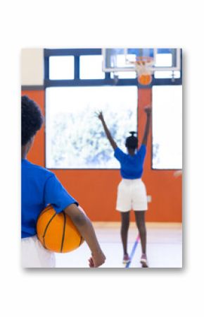 Playing basketball in school gym, diverse girls practicing shooting and holding ball