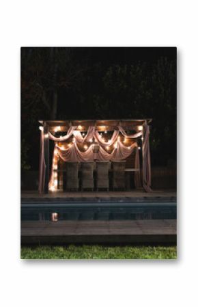 Draped lights on pergola reflecting on pool, creating serene nighttime ambiance