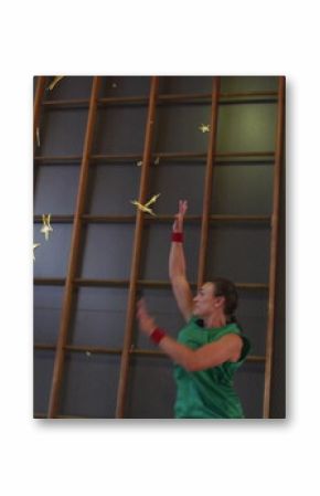 Shooting basketball player in blue uniform releasing ball in gym, hoop, wall bars and star graphics