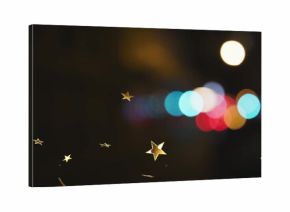 Floating gold star-shaped confetti pieces drifting through nighttime venue, with colorful bokeh