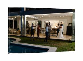 Celebrating joyfully, guests at outdoor wedding reception near pool with string lights