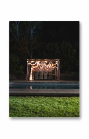 Outdoor pergola beautifully decorated with drapes and lights by pool at night