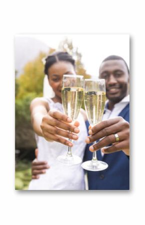 Happy african american bride and groom toasting with champagne at wedding in sunny garden